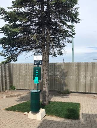 Ground level view of the exterior service area, showing a grassed area with a tree and a waste bag dispenser