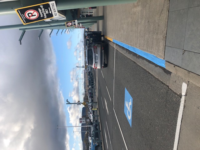 A ground-level view of the curbside assistance area at Thunder Bay Airport, showing the handicap icon on the road and the blue curb